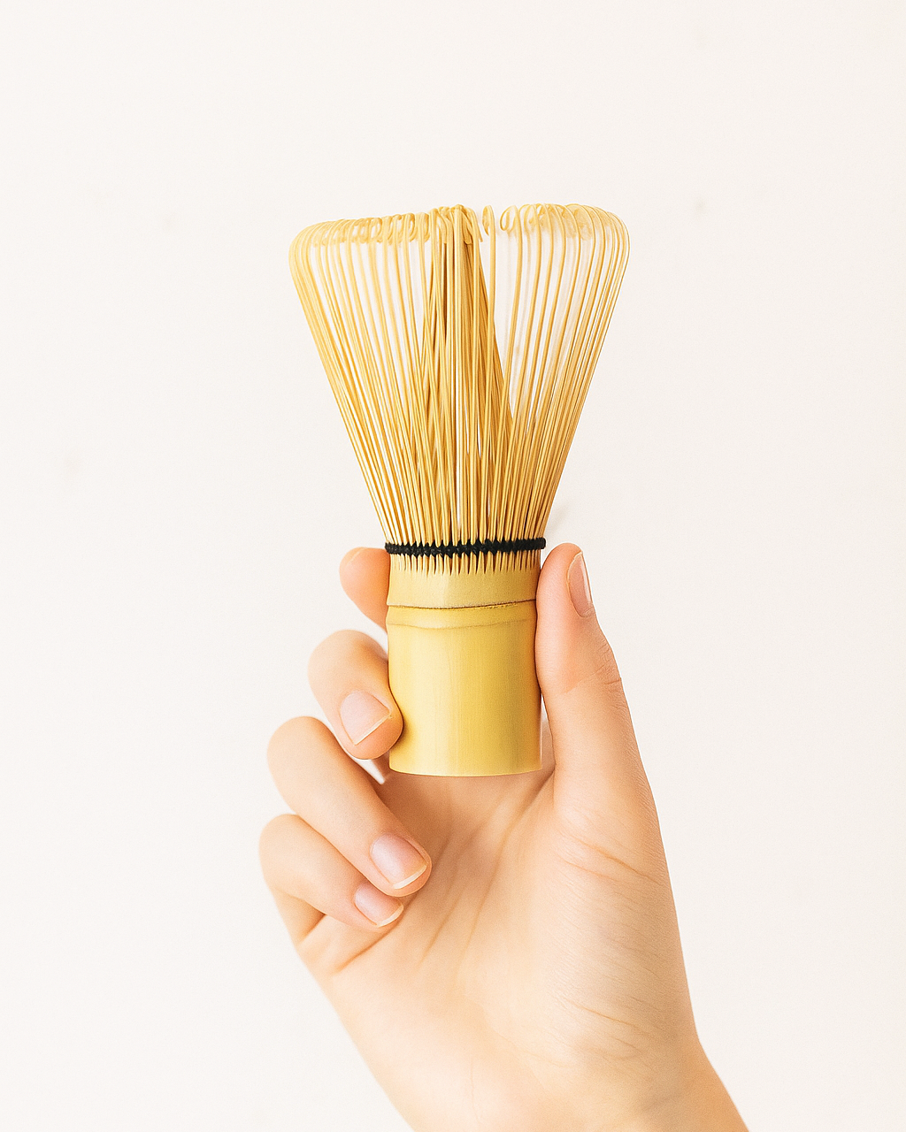 Hand holding a wooden tea whisk against a white background
